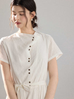 Close-up of the front of a white dress with a diagonal button placket and short sleeves.