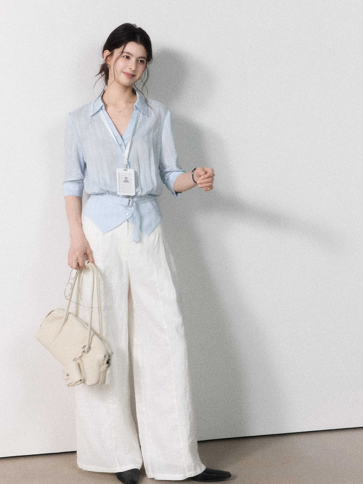 Fitted light blue blouse with collar, button closure, and tied belt.