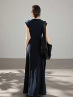 A woman seen from behind wearing a navy blue dress with a waist tie and side pleats.