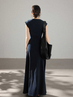 A woman seen from behind wearing a navy blue dress with a waist tie and side pleats.