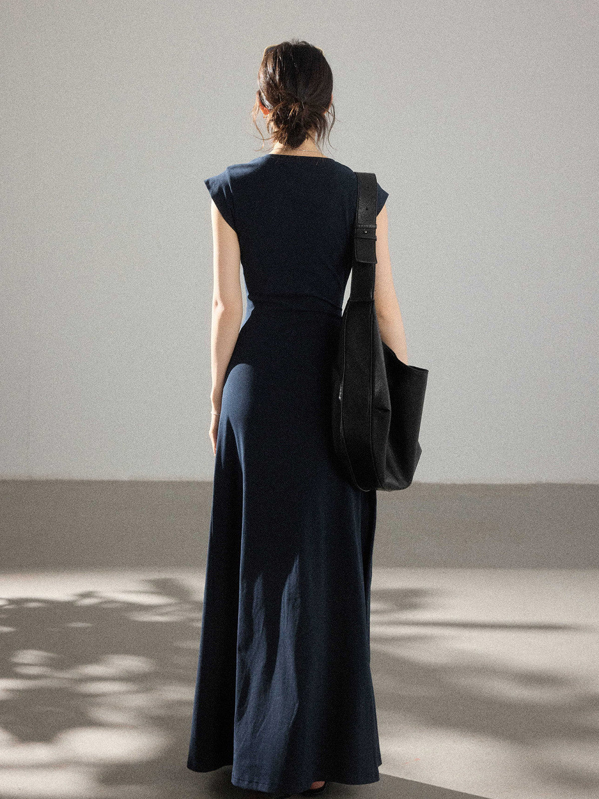 A woman seen from behind wearing a navy blue dress with a waist tie and side pleats.