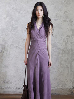 A woman in a purple fit-and-flare maxi dress holding a brown woven bag.