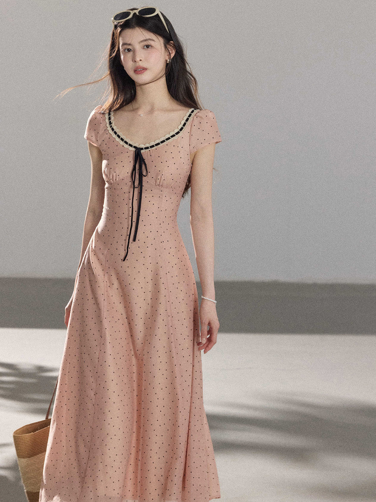 A woman in a pink polka dot dress looking to the side, showing the back tie detail.
