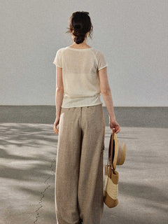 A woman stands with her back to the camera, wearing a cream-colored knitted top with a V-neck and ribbed trim at the hem.