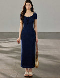 A woman in a navy blue fitted long dress with a square neckline and drawstring detail, standing on a concrete surface.