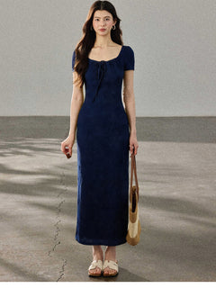 A woman in a navy blue fitted long dress with a square neckline and drawstring detail, standing on a concrete surface.
