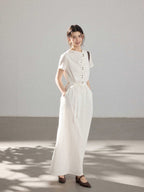 A woman in a white A-line dress with a button placket, tie belt, and brown shoes.