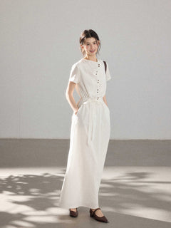 A woman in a white A-line dress with a button placket, tie belt, and brown shoes.
