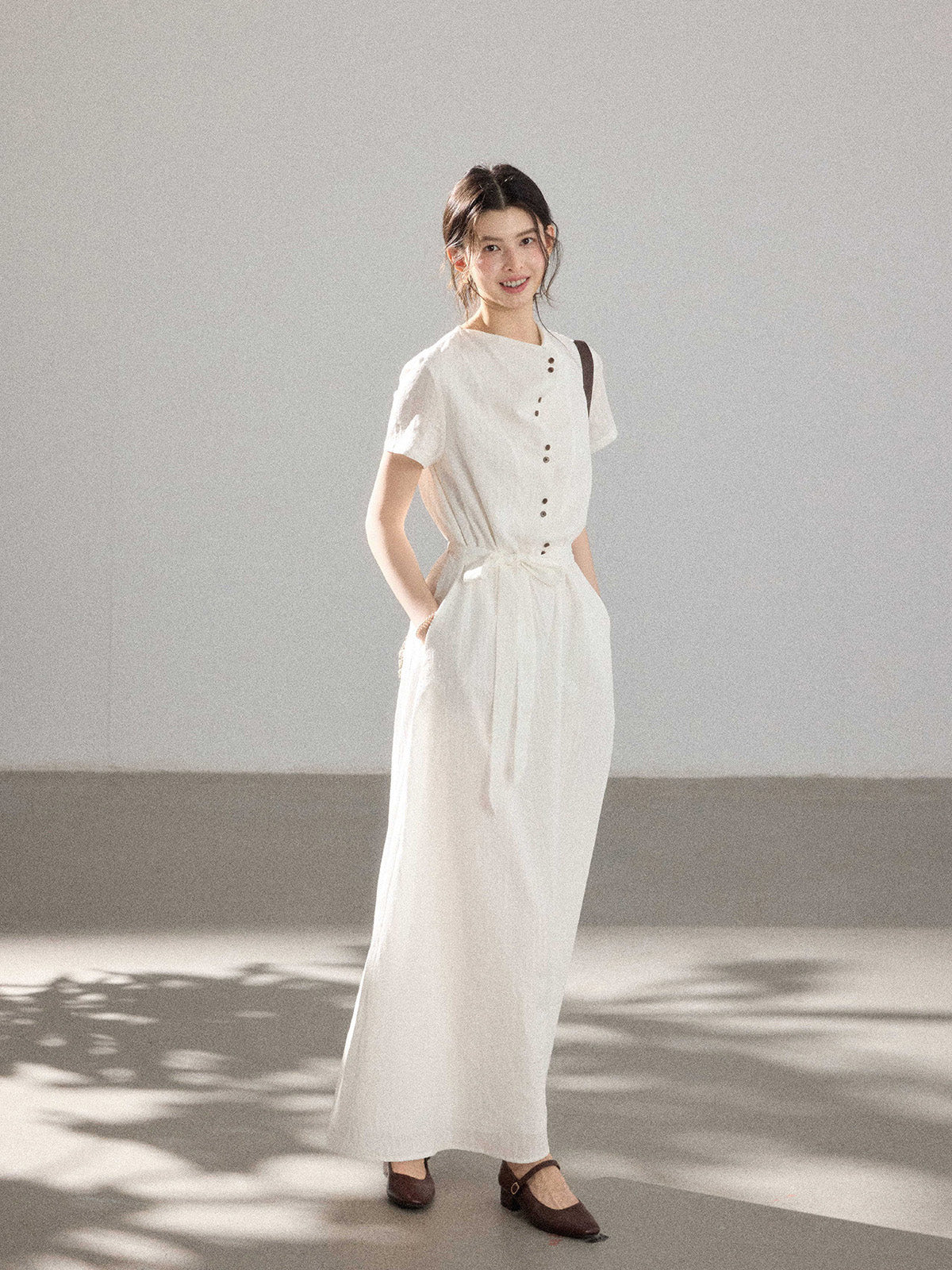 A woman in a white A-line dress with a button placket, tie belt, and brown shoes.