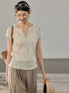 A woman smiles while wearing a cream-colored knitted top with a V-neck and ribbed trim at the hem.