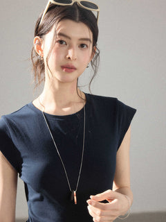 A close-up of a woman wearing a navy blue dress with a round neckline and a long pendant necklace.