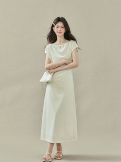 Cream off-shoulder dress featuring draped fabric at neckline and waist, side slit.