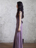 A side profile of a woman wearing a purple sleeveless maxi dress with a back tie belt.