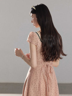 A woman in a pink polka dot dress with lace trim and short sleeves.