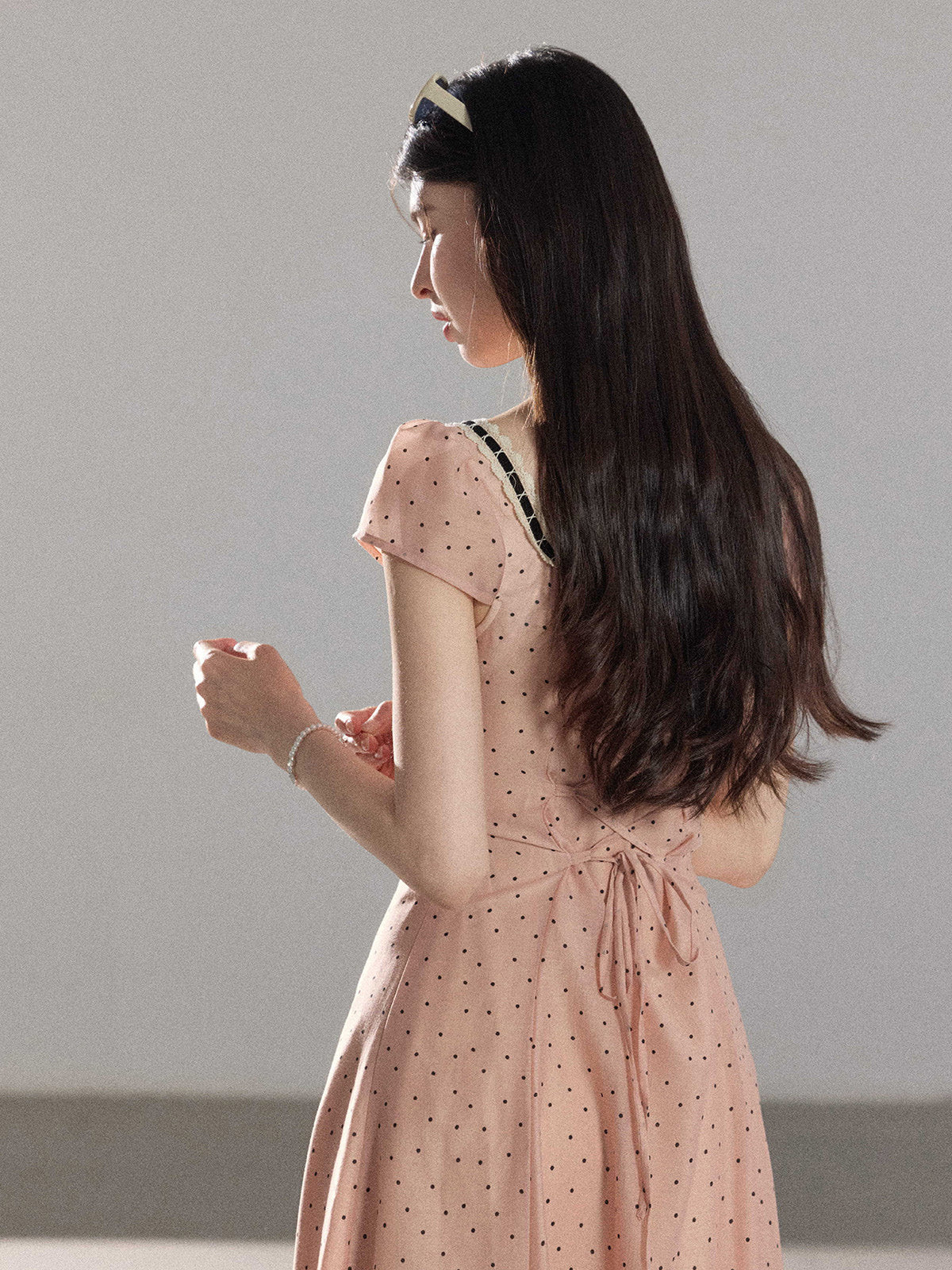 A woman in a pink polka dot dress with lace trim and short sleeves.