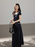 A woman in a black long dress with a square neckline, puff sleeves, and a smocked waist.