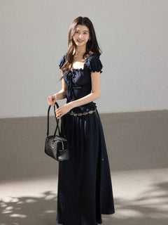 A woman in a black long dress with a square neckline, puff sleeves, and a smocked waist.