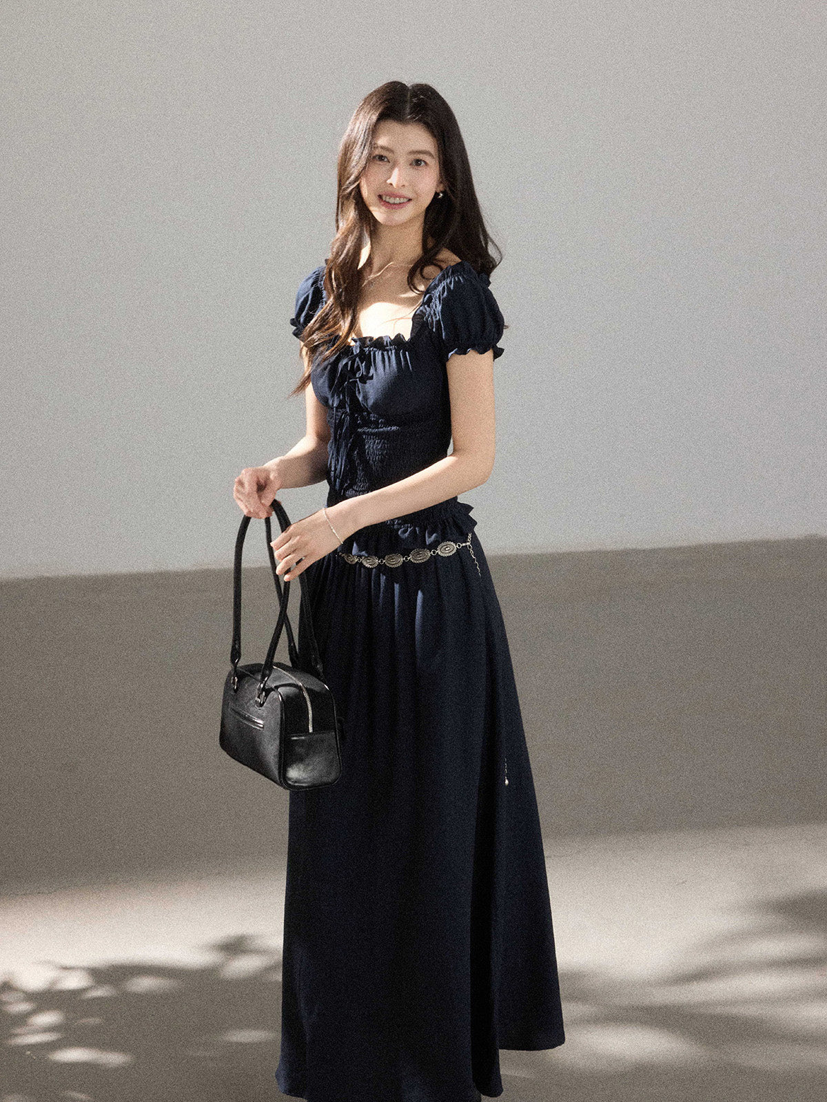 A woman in a black long dress with a square neckline, puff sleeves, and a smocked waist.