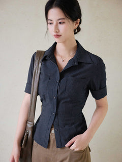 A woman wearing a navy striped fitted top with a collar, button-front closure, cuffed sleeves, and side ties.