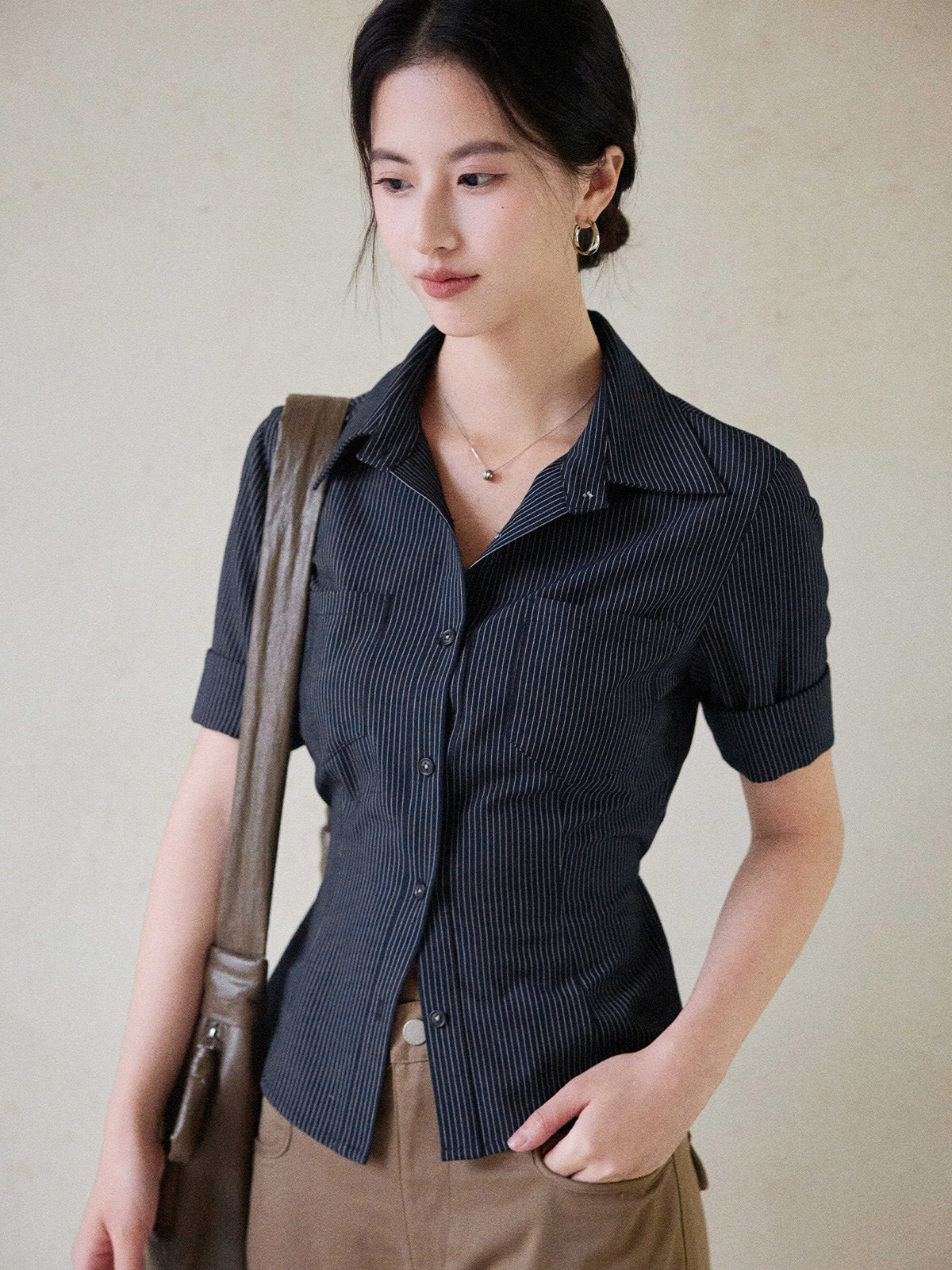 A woman wearing a navy striped fitted top with a collar, button-front closure, cuffed sleeves, and side ties.