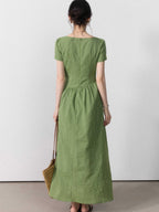 A woman seen from behind wearing a green striped dress with a tie belt and side slit.