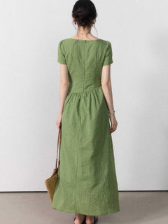 A woman seen from behind wearing a green striped dress with a tie belt and side slit.