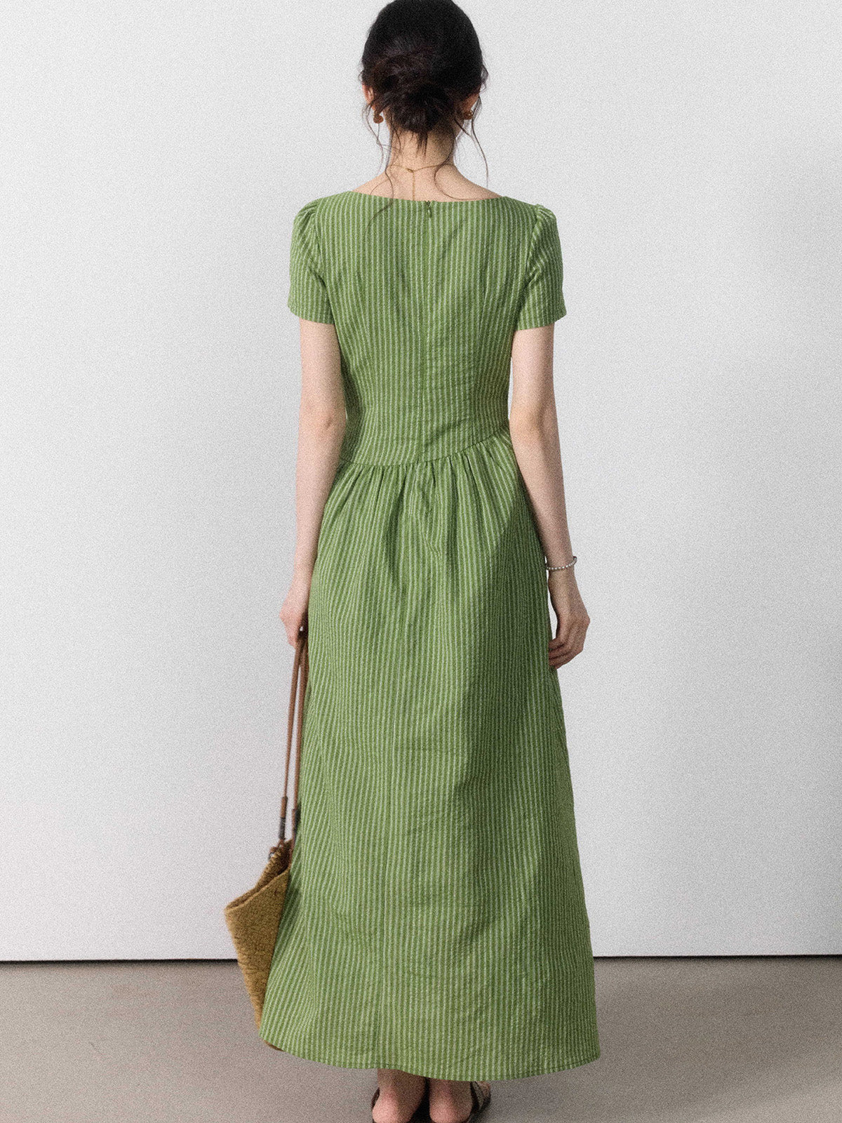 A woman seen from behind wearing a green striped dress with a tie belt and side slit.
