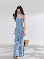A woman in a light blue polka dot long slip dress with ruffled layers and an adjustable strap.