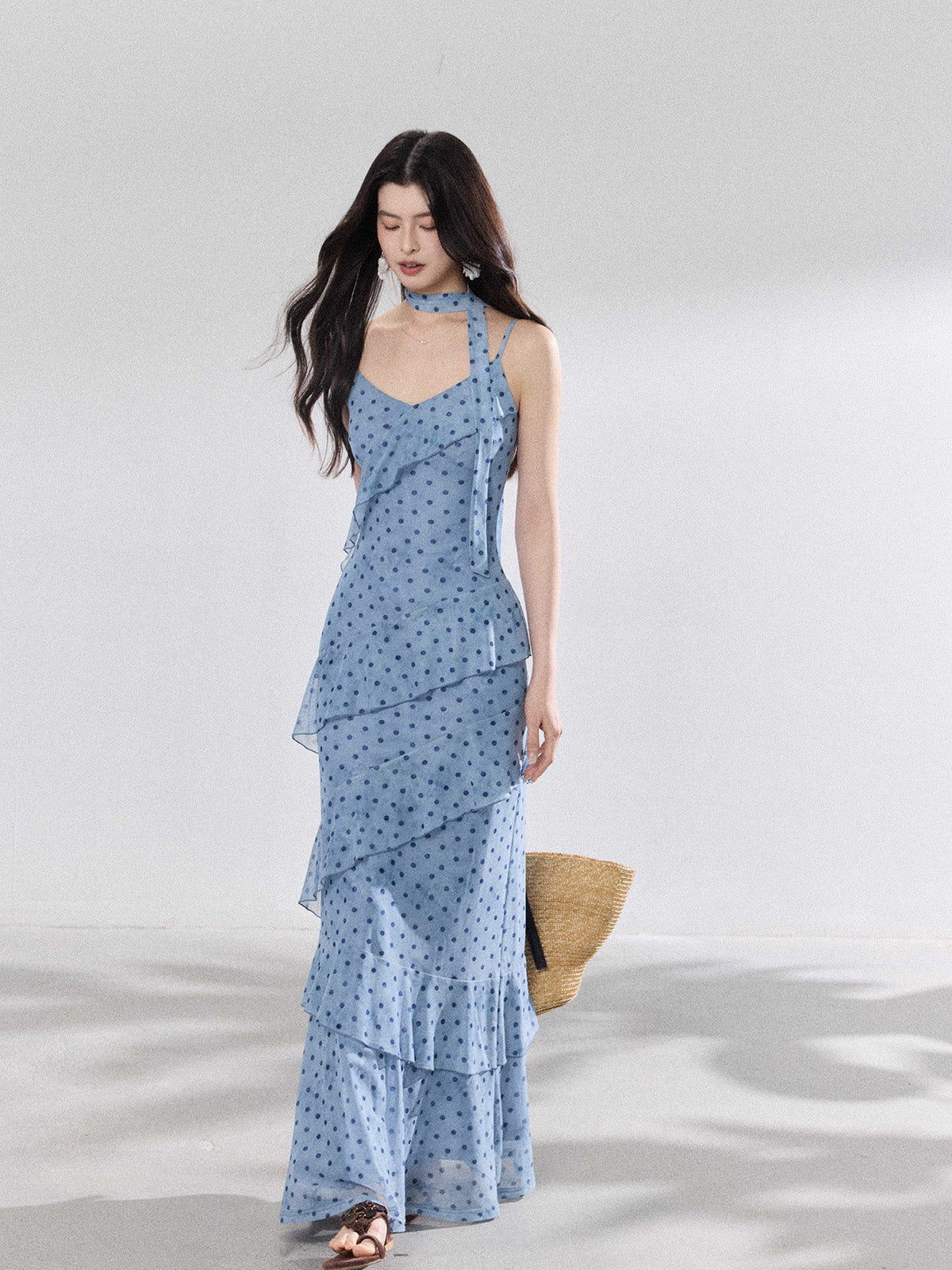 A woman in a light blue polka dot long slip dress with ruffled layers and an adjustable strap.