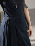 A close-up of the waist tie detail on a navy blue dress with side pleats.
