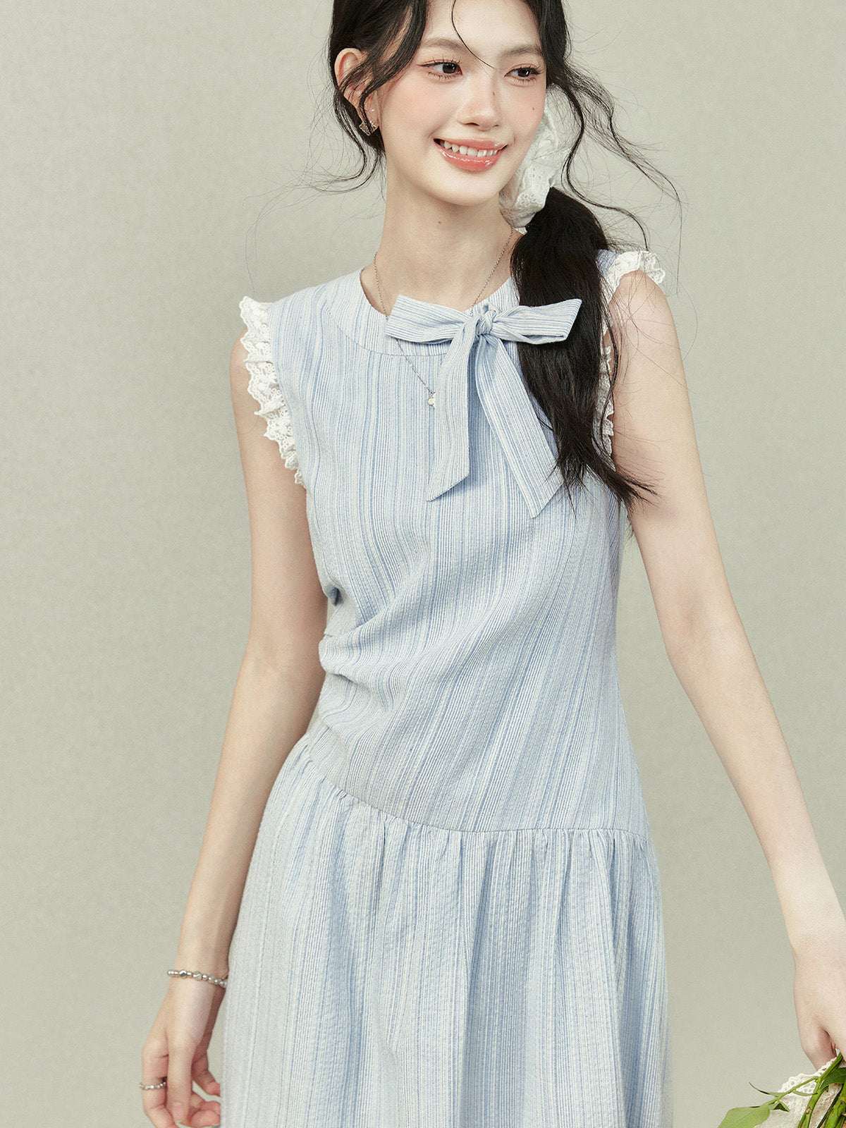 Light blue dress with vertical stripes, lace trim on the shoulders and hem, a bow tie neckline, gathered waist, A-line silhouette, and lace trim.