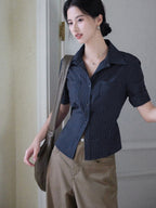 A woman wearing a navy striped fitted top with a collar, button-front closure, cuffed sleeves, and side ties.