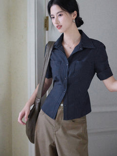 A woman wearing a navy striped fitted top with a collar, button-front closure, cuffed sleeves, and side ties.