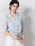 Button-closure light blue blouse with a tied belt at the waist.
