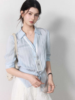 Button-closure light blue blouse with a tied belt at the waist.