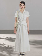 A woman wearing a white A-line dress with a button-front, collar, and twisted waist tie.