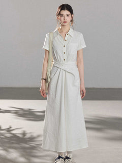 A woman wearing a white A-line dress with a button-front, collar, and twisted waist tie.