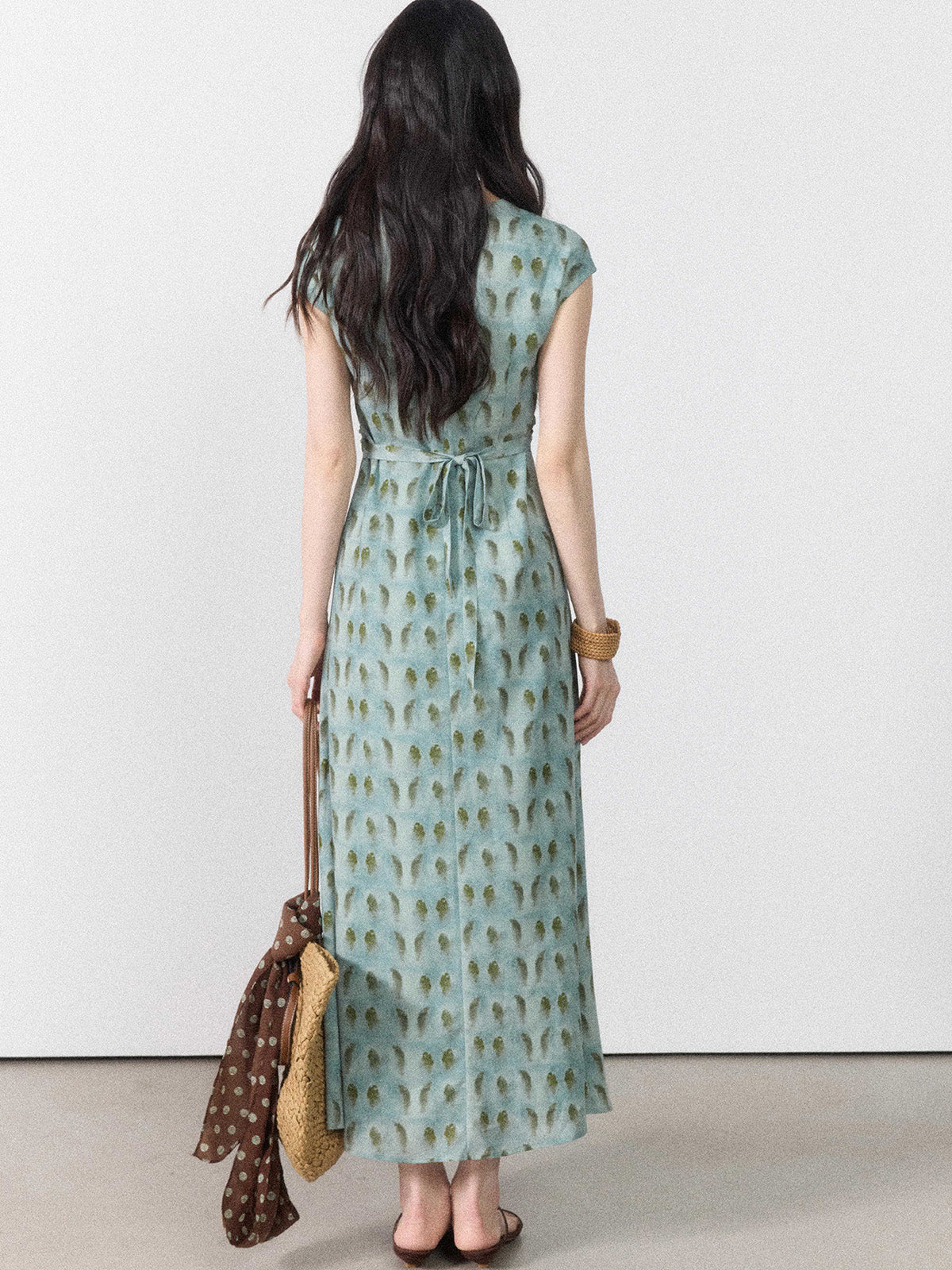 A woman in a long, light blue dress with a green leaf pattern viewed from the back.