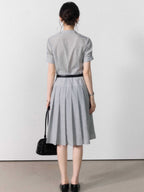 A woman in a grey A-line midi dress with short sleeves, a V-neck collar, and pleated skirt.
