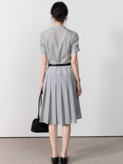 A woman in a grey A-line midi dress with short sleeves, a V-neck collar, and pleated skirt.