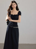 A woman wearing a black long dress with a square neckline, puff sleeves, and a metallic chain belt.