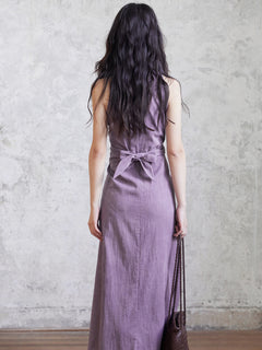 A woman in a purple sleeveless maxi dress seen from behind, showing the back tie belt.