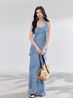 A woman in a light blue polka dot long slip dress with ruffled layers and an adjustable strap.