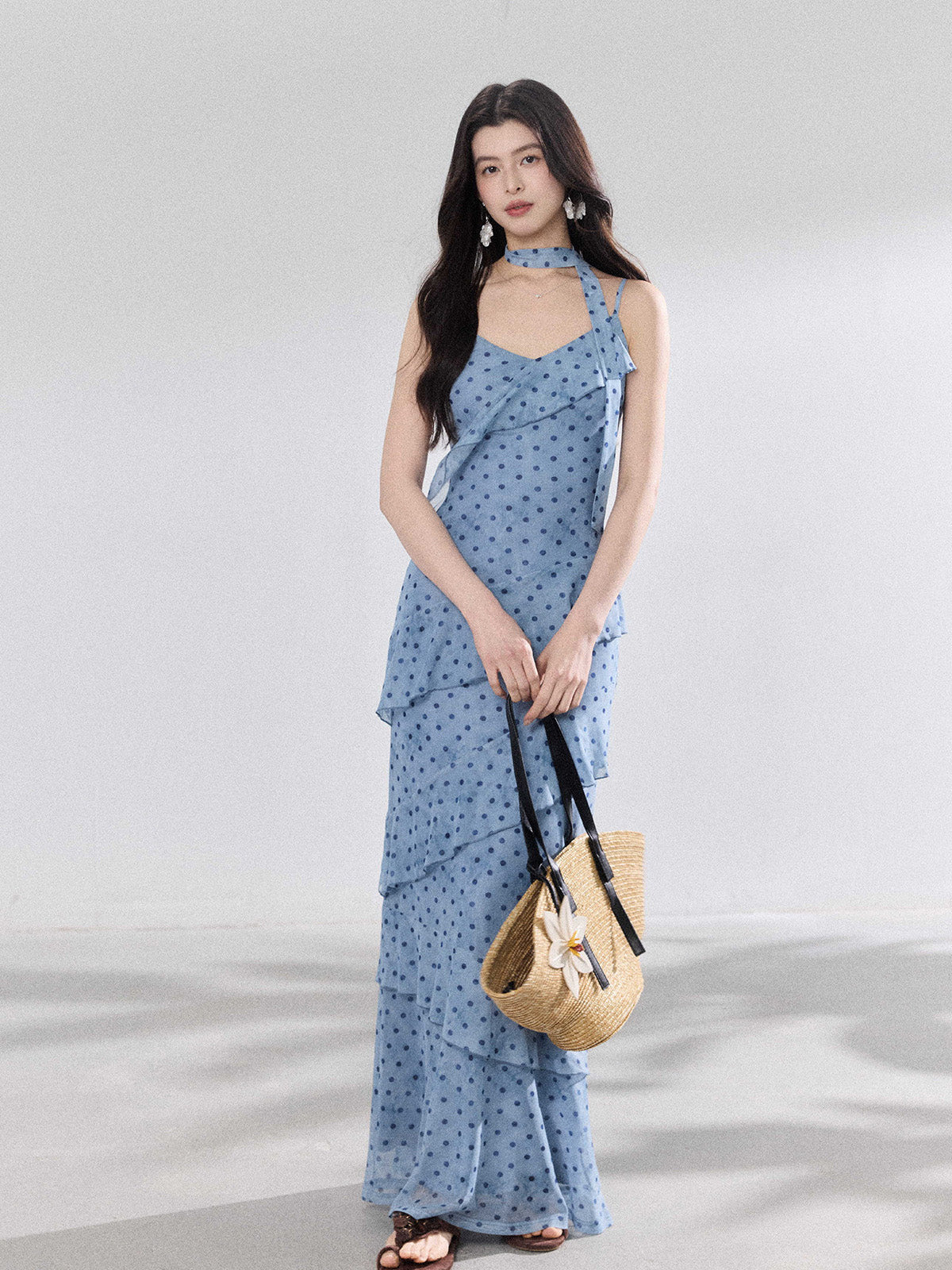 A woman in a light blue polka dot long slip dress with ruffled layers and an adjustable strap.