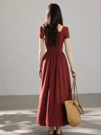 A woman in a red dress with a V-neck and pleated skirt, seen from the back.