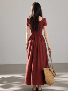 A woman in a red dress with a V-neck and pleated skirt, seen from the back.