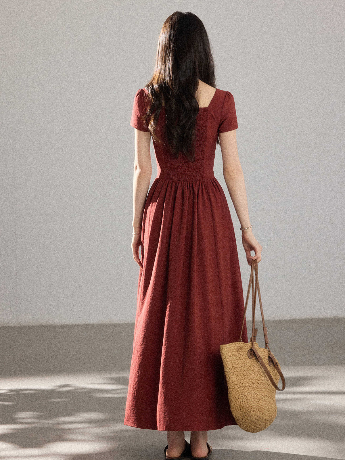 A woman in a red dress with a V-neck and pleated skirt, seen from the back.