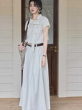A woman wearing an ivory A-line long dress with a diagonal placket and brown belt.