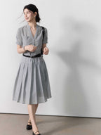 A woman in a grey A-line midi dress with short sleeves, a V-neck collar, and pleated skirt.