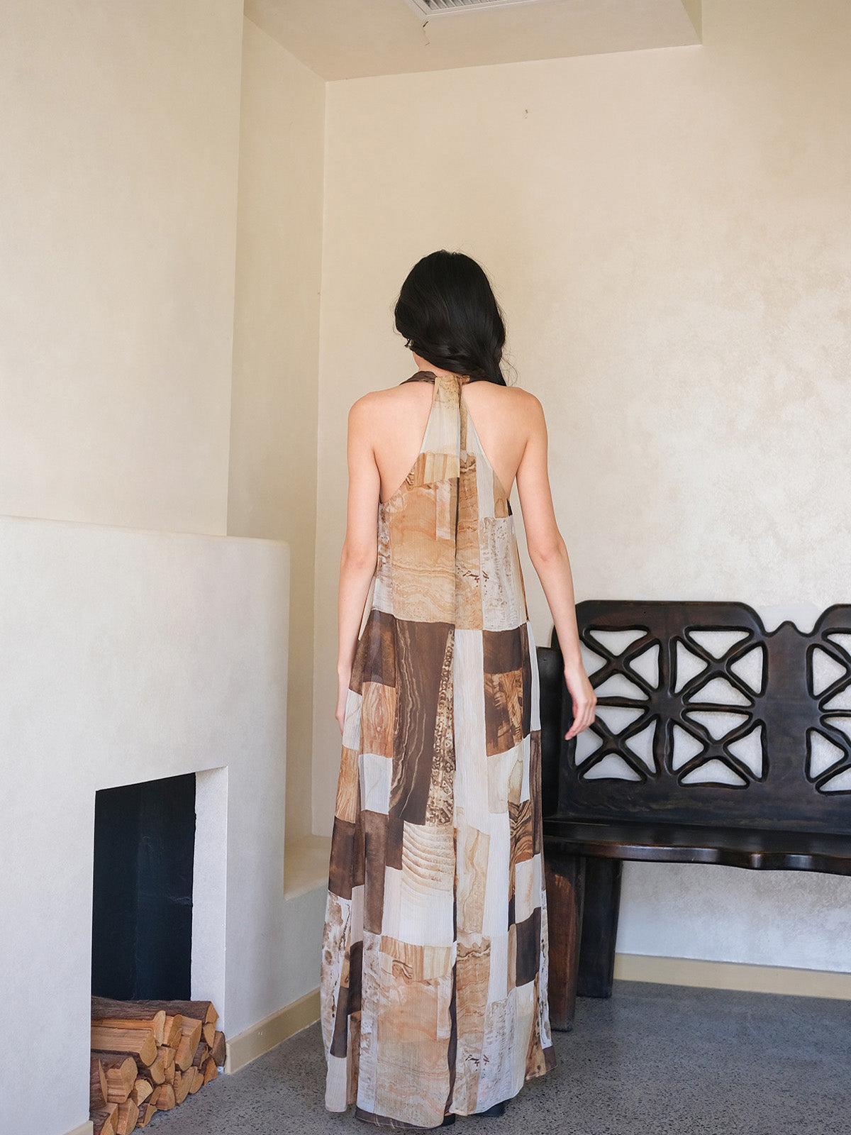 A woman seen from the back, wearing a long dress with a brown and beige patchwork pattern.